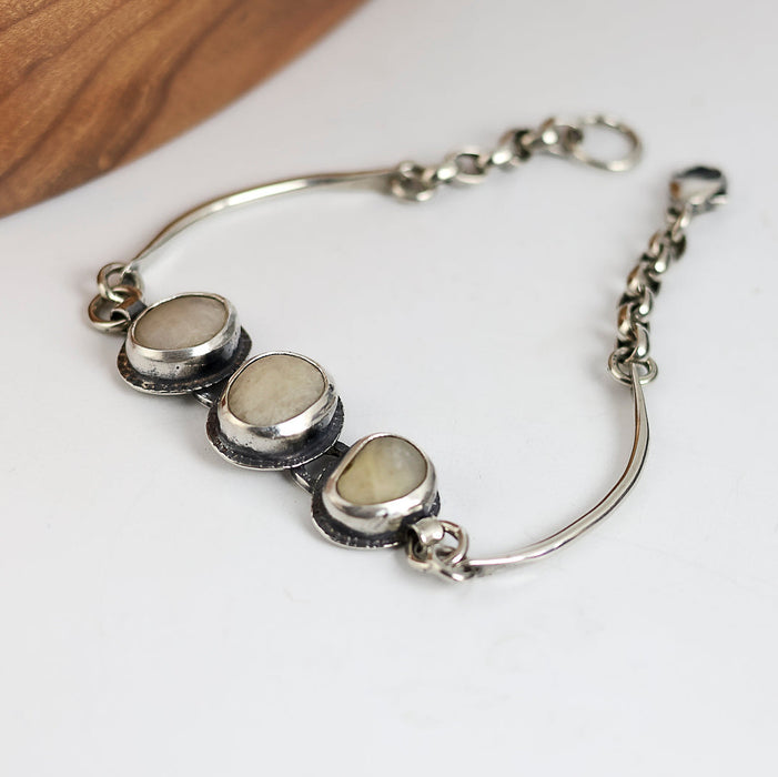 Silver bracelet with three white beach stones on a white surface