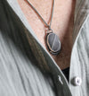 Close-up of a silver pendant necklace with a beach stone on a person wearing a gray shirt.