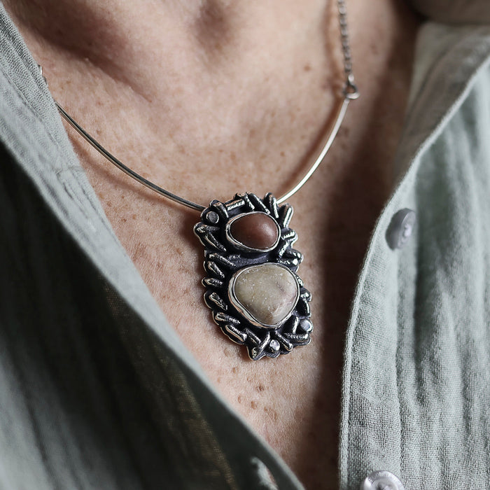 Necklace with a pendant featuring two stones worn by a person.