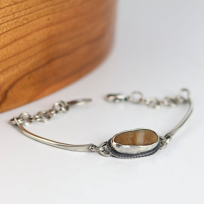 Silver bracelet with a brown stone on a white surface with wooden background