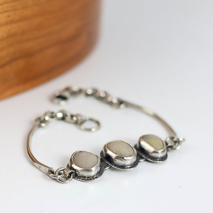 Silver bracelet with three white beach stones on a white surface