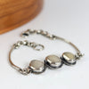 Silver bracelet with three white beach stones on a white surface