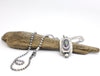 Silver necklace with a pendant on a piece of driftwood against a white background