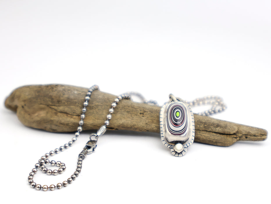 Silver necklace with a pendant on a piece of driftwood against a white background