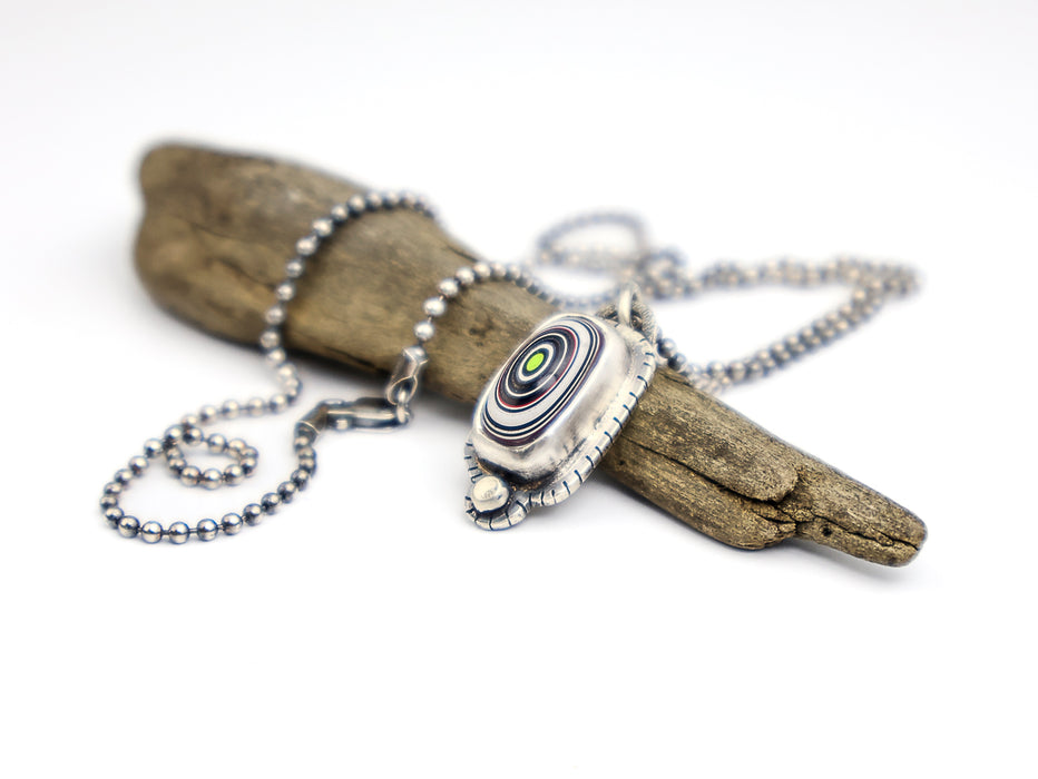 Necklace with a pendant on a piece of driftwood against a white background