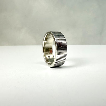 Silver ring with textured band on a white surface