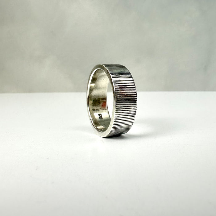 Silver ring with textured band on a white surface