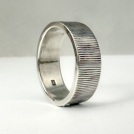 Silver ring with textured band on a white background