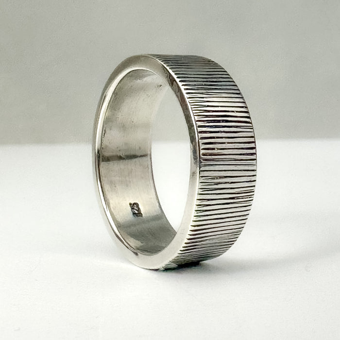 Silver ring with textured band on a white background