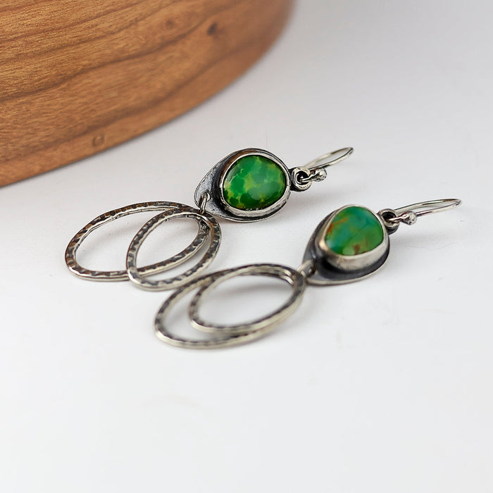 Silver earrings with green gemstones on a white surface
