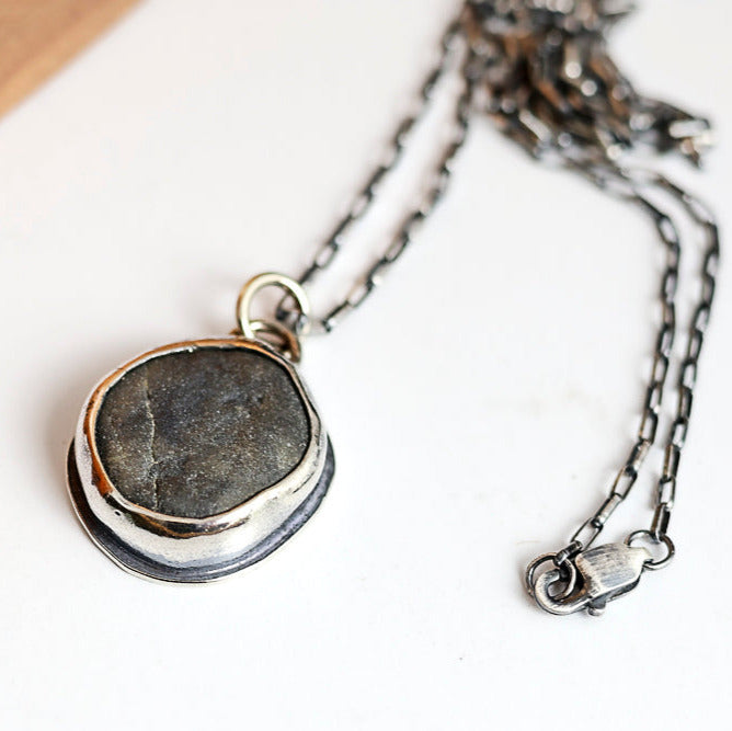 Necklace with a pendant featuring a dark beach stone on a white background