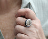 Hand wearing a silver ring with a dark band, blurred background