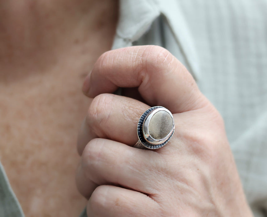 Hand wearing a silver ring with a dark band, blurred background