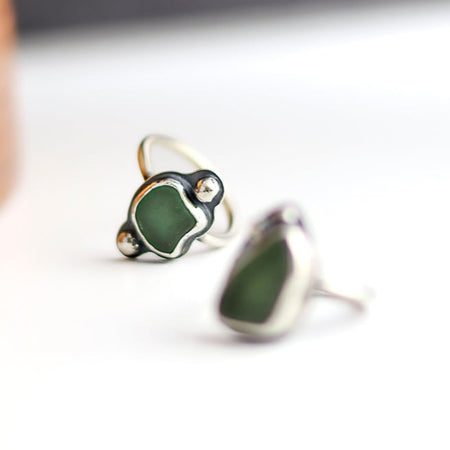 Two green sea glass rings with silver settings on a white background