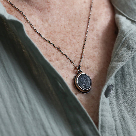 Necklace with a pendant on a person wearing a light-colored shirt.