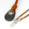 A dark gray stone pendant with a silver grommet threaded onto a tan leather cord with silver clasp, shown on a white background.