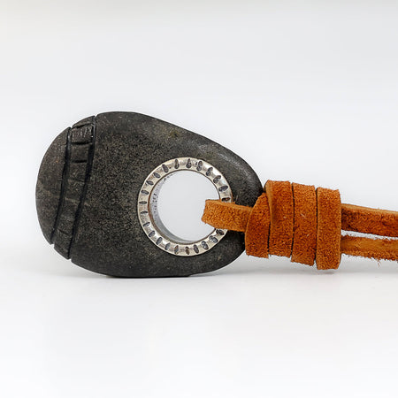 Dark grey teardrop shaped Cape Cod beach stone pendant with a hand carved checkered pattern running around the entire perimeter, a sterling silver grommet bail with line texture drilled through the top, on a natural tan suede cord on a white background.