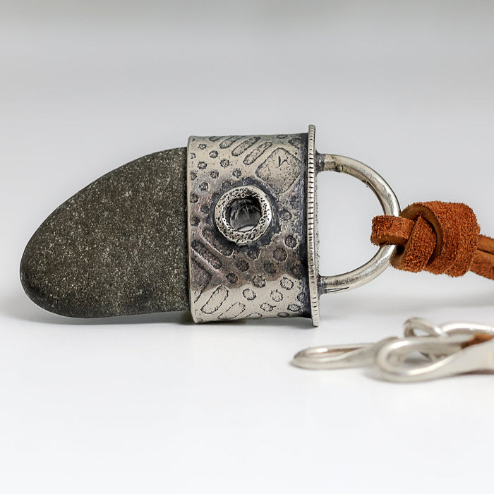 beach stone pendant with a silver textured end cap on a brown suede cord