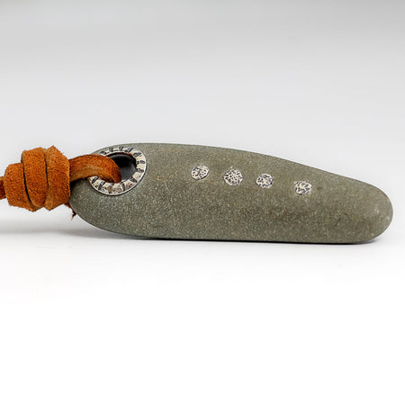 A  gray stone pendant featuring a silver grommet and four small silver granules attached to an orange-brown leather cord, shown on a white background.