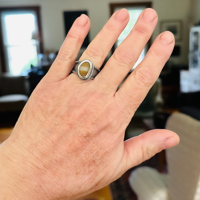 Hand wearing a ring with a yellow stone in an indoor setting