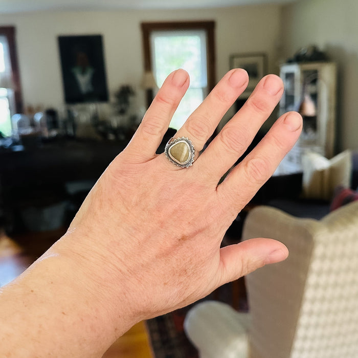 Hand wearing a ring with a beach  stone in a room setting