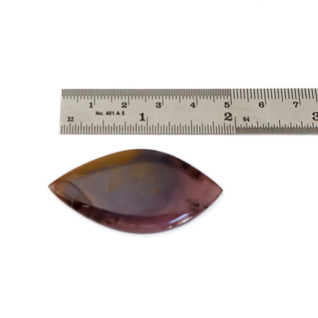 An oval shaped agate cabochon gemstone with brown, purple, and amber, shown below a metal ruler for scale on a white background.