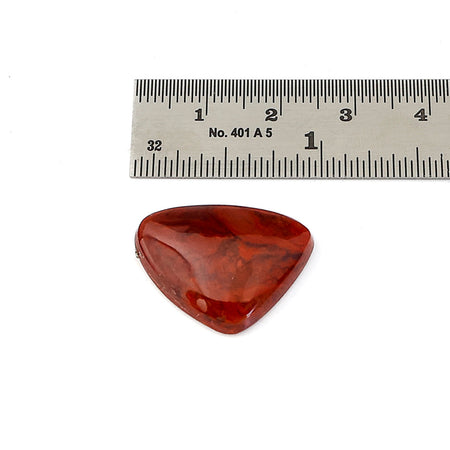 A polished red agate cabochon with natural marbled patterns, shown below a metal ruler for scale on a white background.
