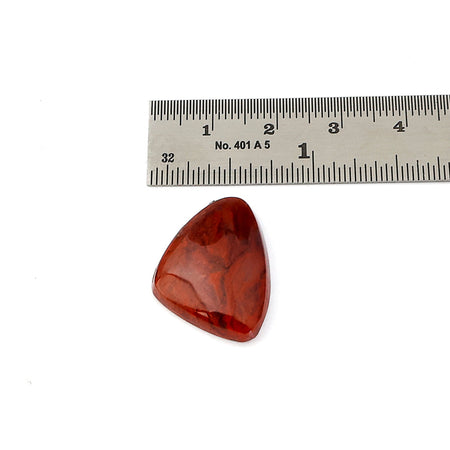 A triangular red agate cabochon with natural marbled patterns, shown below a metal ruler for scale on a white background.