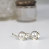 A pair of sterling silver earrings with round iridescent coin pearls, displayed on a white surface with a softly blurred glass jar in the background.