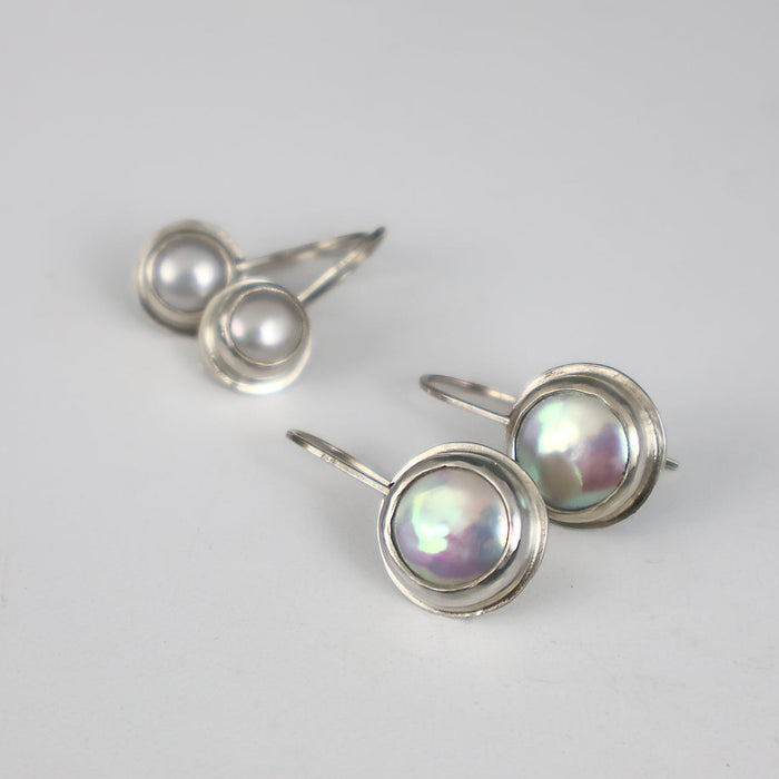 Two pairs of sterling silver earrings with round iridescent coin pearls, displayed on a white surface.