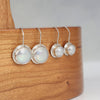 Two pairs of sterling silver earrings with round iridescent coin pearls, displayed on a wood surface.
