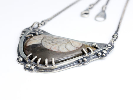 Silver necklace with a pendant featuring a ammonite fossil  on a white background