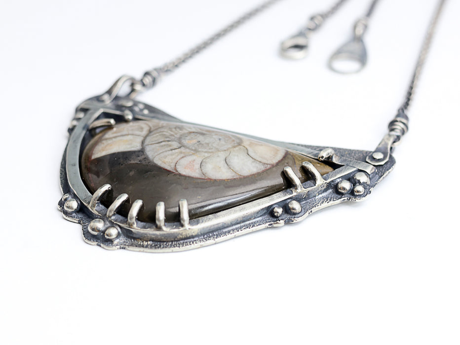 Silver necklace with a pendant featuring a ammonite fossil  on a white background
