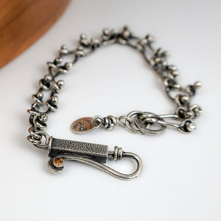 Sterling silver chain bracelet with a citrine in a tube setting, photographed on a white surface with a wooden edge in the corner.