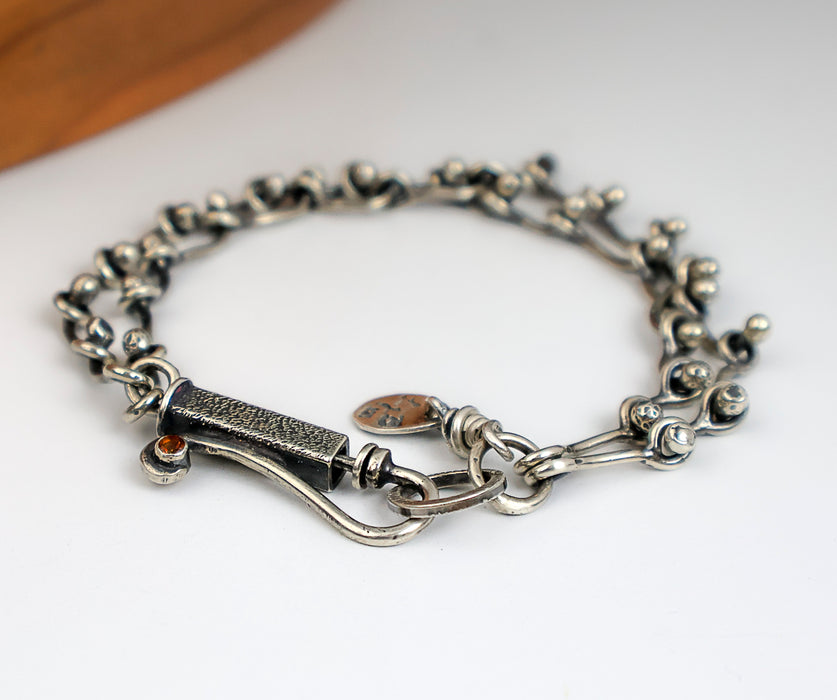 Sterling silver chain bracelet with a citrine in a tube setting, photographed on a white surface with a wooden edge in the corner.