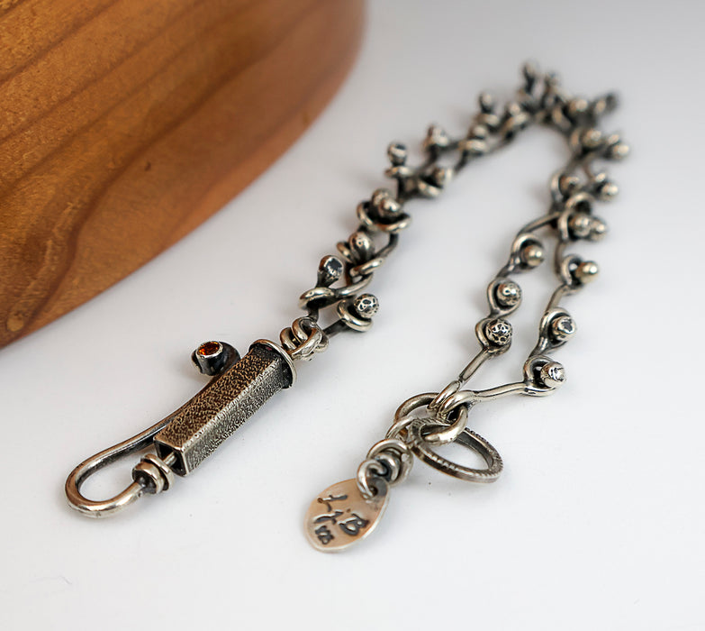 Sterling silver chain bracelet with a citrine in a tube setting, photographed on a white surface with a wooden edge in the corner.