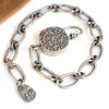 A silver chain bracelet with elongated oval links, twisted rope details at the link joints, a round toggle,  displayed on a white background with a wooden surface in the corner.