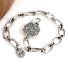 A silver chain bracelet with textured oval links, a round textured toggle, displayed on a clean white background.