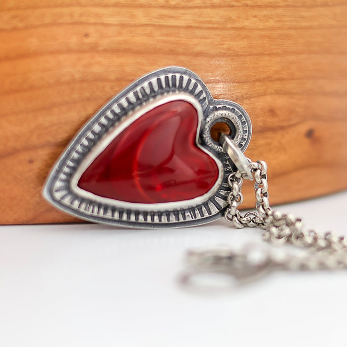Heart-shaped pendant with red center and silver border on a wooden background