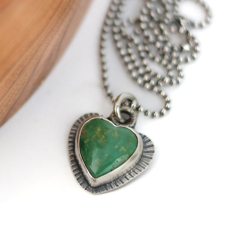 Heart-shaped green stone pendant on a silver chain against a white background