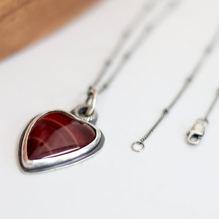 Heart-shaped pendant with red stone on a silver chain against a white background