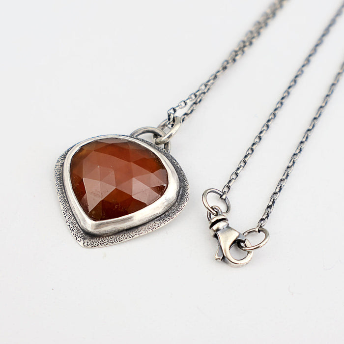 Handmade sterling silver pendant with dark orange rose cut hessonite garnet set point down, sand textured border, on an oval rolo chain