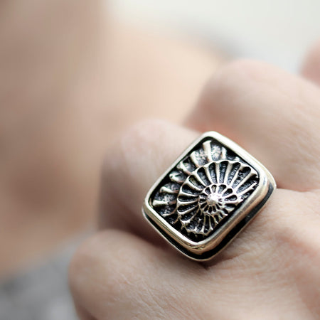 Silver ring with intricate design worn on a finger against a blurred background