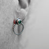 Close-up of an ear with a silver earring featuring a malachite gemstone on a neutral background