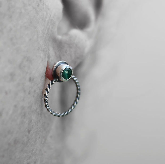 Close-up of an ear with a silver earring featuring a malachite gemstone on a neutral background