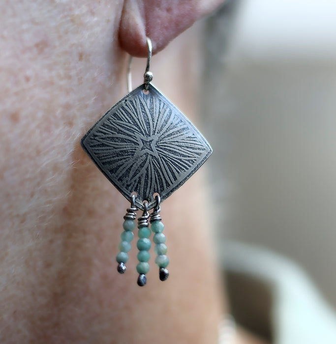 Silver earring with textured design and dangling beads worn on an ear.