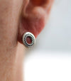 Silver earring worn on an ear with a plain background