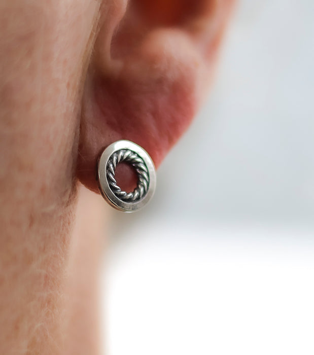 Silver earring worn on an ear with a plain background