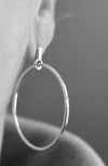 Silver hoop earring worn on an ear with a blurred background