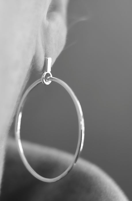 Silver hoop earring worn on an ear with a blurred background